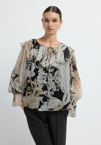 Blusa trasparente con stampa floreale e paisley nei toni del beige, nero e grigio, con scollatura arricciata e maniche a sbuffo, abbinata a pantaloni a righe neri.