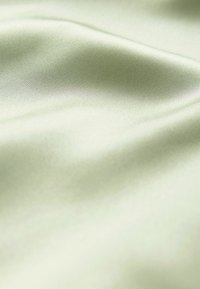 Satin audums gaiši zaļā krāsā ar gludu tekstūru, ar maigu spīdumu un maziem krokām, radot mīkstu drapēšanas izskatu.
