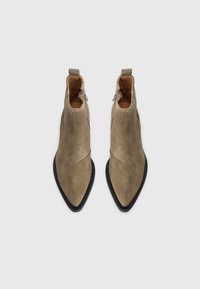 Botines de ante marrón claro con punta afilada, que presentan una suela negra y un discreto detalle de cremallera en el costado.