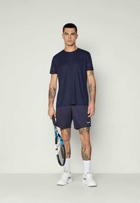 Navy zils īsām piedurknēm sporta krekls kopā ar saskaņojošām šortiem. Apģērbs izceļas ar vienkāršu dizainu, ar teksturētu apdari un logotipa akcentiem.