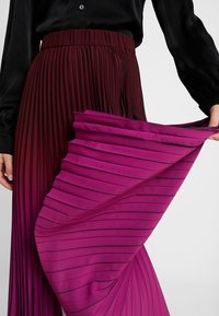 Plissierter Rock mit Farbverlauf in Burgunderrot und Rosa. Texturiertes Gewebe mit vertikalen Falten und einem glatten Bund.