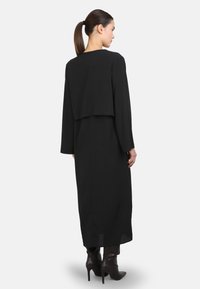 Langes schwarzes Kleid mit einem Design der obersten Schicht, das lange Ärmel und eine glatte Textur aufweist, kombiniert mit spitzen braunen High Heels Stiefeln.