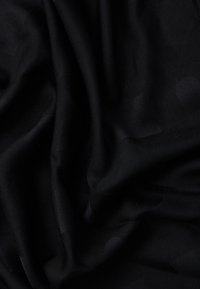 Tejido negro con textura suave, que presenta patrones tonales sutiles y pliegues drapeados, creando profundidad y variación en la apariencia de la superficie.