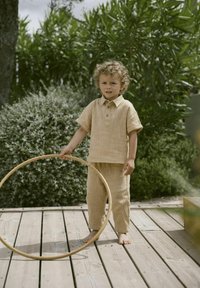 Helebeež, tekstureeritud puuvillane komplekt, mis sisaldab lühikeste varrukate ja krae ning nööbiga särki ning vasteid lahti lõigatud pükse. Laps hoiab puust rõngast.