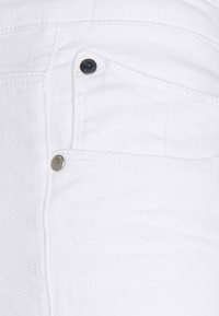 White denim fabric close-up showcasing a front pocket with metal detailing and stitching, featuring a smooth texture and crisp design.