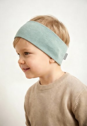 Toddler with light brown hair wears a wide light blue headband and beige sweater, looking left with a slight smile, against a plain background.