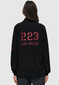Svart fleece-pullover med stora röda tryckta siffrorna "223" och texten "OFF PITCH" på baksidan, med långa ärmar och krage.