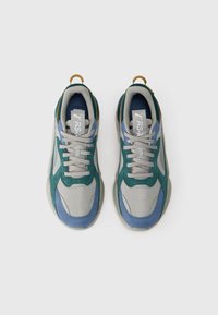 Puma RS-X sporta apavi pelēkā, zaļā un zilā krāsā ar bēšām šņorēm, skatīti no augšas uz baltas fona.