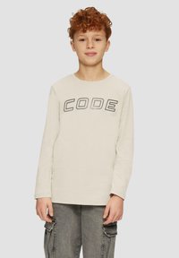 Weißes Langarm-T-Shirt mit dem Wort "CODE" in fetter schwarzer Schrift auf der Brust, kombiniert mit grauen Cargo-Hosen.