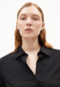 Camicia nera con colletto, realizzata in tessuto liscio e leggermente lucido, con dettagli visibili del colletto e della parte frontale.