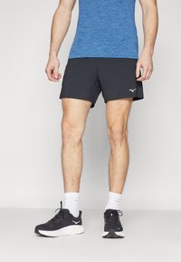 Schwarze sportliche Shorts aus feuchtigkeitstransportierendem Material, knielang, kombiniert mit schwarzen Laufschuhen, weißen Socken und einem blauen Sportshirt.