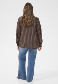 Bruine gestreepte blouse met lange mouwen, knoopmanchetten en een losse pasvorm, gecombineerd met blauwe flared jeans. Glad stoftextuur.