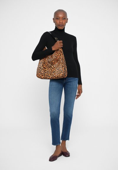 Borsa a tracolla con stampa leopardata in arancione e nero, texture morbida, design hobo grande, tenuta da una persona che indossa un dolcevita nero e jeans blu.