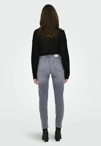 Šedé džíny s vysokým pasem a rovnými nohavicemi, doplněné černým svetrem s otevřeným úpletem. Obsahují zadní nášivku a design s pěti kapsami.