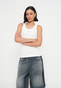 Λευκό ριμπ αμάνικο τοπ με στρογγυλή λαιμόκοψη και μικρό ασημένιο λογότυπο. Συνδυασμένο με άνετα, ξεβαμμένα μπλε denim σορτς.