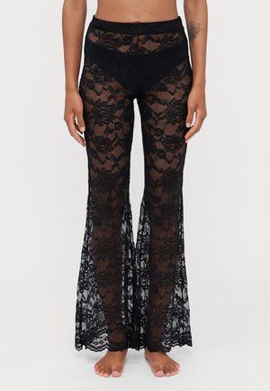 Black lace flared pants featuring floral patterns, semi-sheer texture, a fitted waistband, and wide openings from knees to hem.