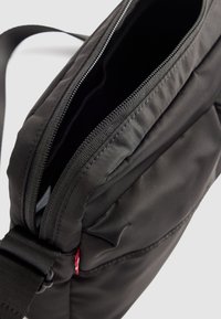 Borsa a tracolla nera con cerniera aperta e tracolla regolabile, che mostra la texture del tessuto e i dettagli delle cuciture, su uno sfondo bianco.