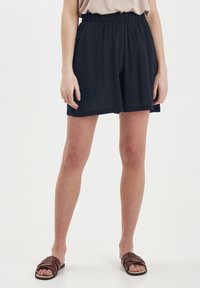 Mörkblå shorts med resår i midjan, lös passform och lätt textur. Bärs med bruna platta sandaler.