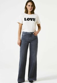 Witte t-shirt met "LOVE" in zwarte letters, gecombineerd met high-waisted, wijde donkere denim jeans. Beide items hebben een eenvoudig ontwerp.