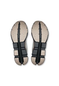 Semelles de sneakers noires et beiges avec des motifs texturés, des sections segmentées et une barre de stabilité noire centrale. Présente le marquage "Cloudtec".