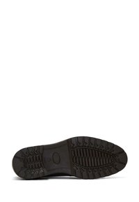 Suela de zapato de goma negra con un patrón de textura, que incluye surcos profundos y crestas para una mayor tracción. Logo circular cerca del área del arco.