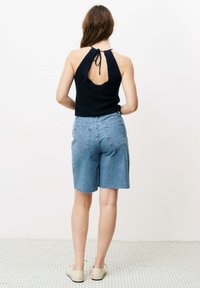 Schwarzes Oberteil mit Neckholder und Rückenschnürung, offene Rückendetails, kombiniert mit hellblauen Jeansshorts mit fransigem Saum und zwei Gesäßtaschen.