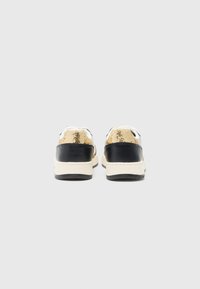 Black and gold sneakers with a textured gold upper, black leather heel, and cream sole. Features white laces and subtle stitching details.