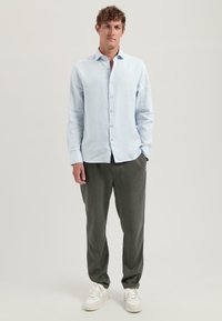 Camisa de lino azul claro de manga larga con cuello abotonado, combinada con pantalones gris oscuro de corte relajado y zapatillas blancas.