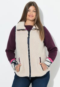 Beige Fleece-Weste mit Reißverschluss, Seitentaschen und Ärmeln in lila, marineblau und pink, die ein schwarz-weißes Muster zeigen.
