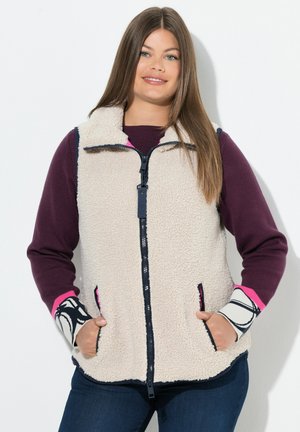 Beige Fleece-Weste mit Reißverschluss, Seitentaschen und Ärmeln in lila, marineblau und pink, die ein schwarz-weißes Muster zeigen.