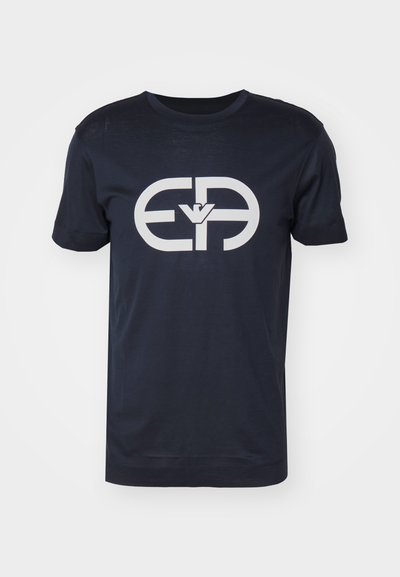 Tamsiai mėlynas medvilninis marškinėliai, trumpomis rankovėmis, apvalia iškirpte. Priekyje yra didelis baltas logotipas, lygus apvadas ir standartinė forma.