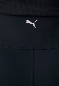 Gros plan d'une ceinture de vêtement de sport noire avec le logo Puma blanc centré au-dessus de la couture cousue.
