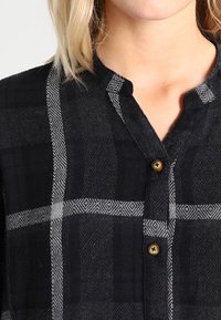 Camicia a quadri nera e grigia con colletto, tessuto texturizzato e un sottile motivo geometrico, completa di bottoni dorati.