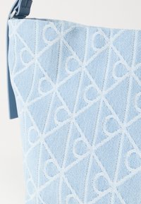 Τσάντα χειρός ανοιχτού γαλάζιου χρώματος με υφή υφάσματος, σε λευκό γεωμετρικό σχέδιο από τρίγωνα και σχήματα καρδίας.