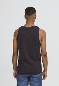 Black sleeveless tank top with a round neckline, made of soft fabric. Simple design, no patterns, paired with blue denim jeans.