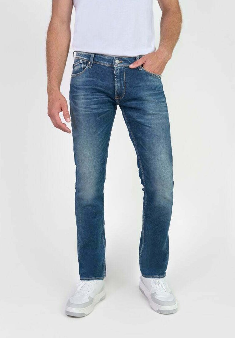 Vaqueros de mezclilla azul con un acabado desgastado, corte recto, diseño de cinco bolsillos y detalles de costura clara, combinados con zapatillas blancas.