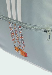 Svjetlosiva platnena torba s džepom na patentni zatvarač, ukrašenim pikseliziranim grafičkim dizajnom u narančastim, crvenim i crnim nijansama. Tri bijele pruge na vrhu.