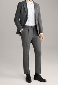 Grau gemusteter Anzug mit einem Blazer mit Revers und maßgeschneiderten Hosen. Kombiniert mit einem weißen Button-up-Hemd und schwarzen Lederschuhen.