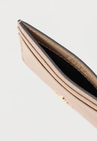 Vaaleanbeige nahkainen lompakko, jossa on sileä pinta, kultaiset metalliosat ja tumma sisusta. Avattuna sisäosan yksityiskohtien esittelemiseksi.