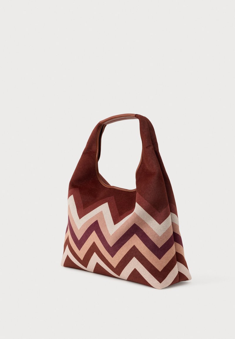 Sac en tissu doux avec un motif en zigzag dans des nuances de bourgogne, rose et crème. Il dispose d'une grande poignée courbée et d'un design spacieux.