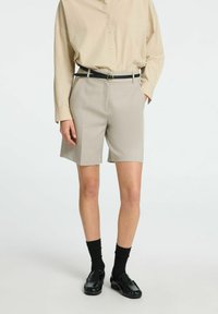 Beige skræddersyede shorts med en glat tekstur, der har en mellemhøj talje, sidelommer og er stylet med et sort bælte og loafers.