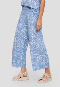 Světle modré kalhoty širokého střihu s bílými květinovými vzory, obsahující pohodlný pas a texturovanou látku. Spárováno s béžovými pletenými sandály.