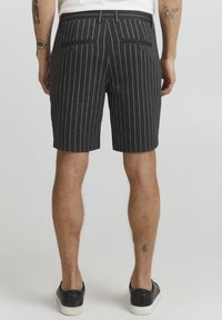 Pantaloni corti a righe grigio scuro realizzati in tessuto leggero. Presentano due tasche posteriori e un taglio dritto, con una vita piatta. Adatti per il clima caldo.