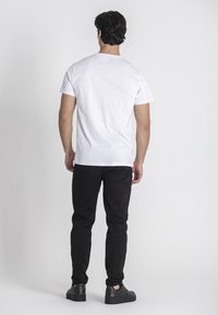 Camiseta blanca de mangas cortas, material de algodón, diseño liso sin gráficos, combinada con jeans negros, detalles de costura visibles, y zapatillas negras.