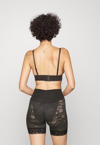 Svart underklädesset som innehåller en bralette med spetsdetaljer och justerbara strappar samt högmidjade shorts med genomskinliga spetspaneler.
