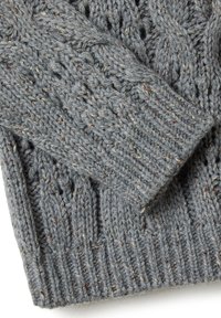 Gros plan sur un tissu tricoté gris plié avec des fils métalliques cuivrés tissés tout au long, montrant des motifs en côte et en câble texturés.