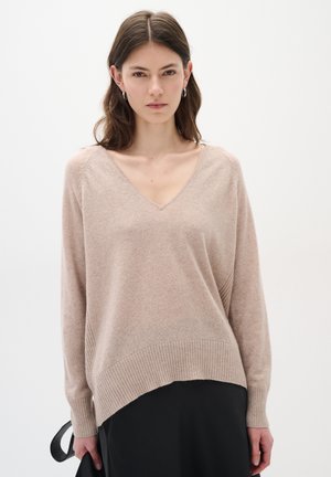 Lys beige V-hals sweater lavet af blødt strikstof, med ribkant og afslappet pasform. Lange ærmer med tapered manchetter.