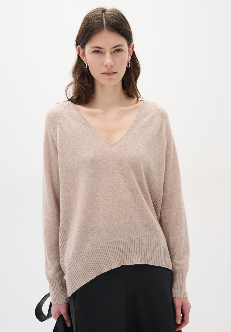 Hellbeige V-Ausschnitt-Pullover aus weichem Strickstoff, mit geripptem Saum und lockerer Passform. Lange Ärmel mit schmalen Bündchen.