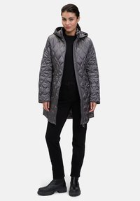 Grijze, gewatteerde, gevoerde jas met een ritssluiting aan de voorkant, zijzakken en een langere snit. Draag het over een zwarte top en zwarte broek, gecombineerd met zwarte laarzen.