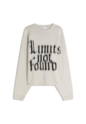 Světle béžový svetr s dlouhým rukávem, na přední straně s černým rozmazaným textem "Limits for Edmio" ve stylizovaném písmu, s žebrovanými manžetami a límcem.